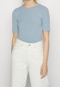 Ljusblå t-shirt med korta ärmar i mjukt tyg, kombinerad med högmidjade vita denimjeans med knappar och traditionella fickor.