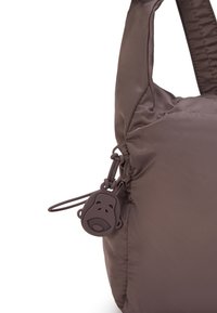 Sac à main rembourré marron avec une texture de tissu doux, doté d'un petit porte-clés en caoutchouc en forme de visage de singe attaché à la fermeture éclair latérale.