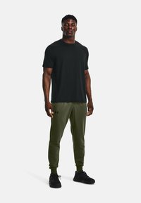 Svart t-shirt med kort ärm i kombination med olivgröna joggers med elastisk midja och svart accentlogotyp. Svarta träningsskor fulländar outfiten.