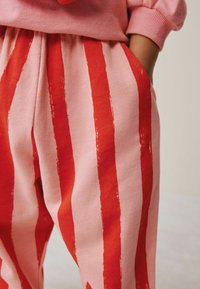 Pink sweatpants with bold red vertical stripes and pockets. Fabric is soft and slightly stretchy, featuring a relaxed fit design.