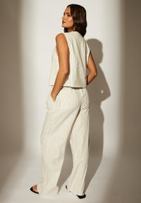 Conjunto de dos piezas a rayas blancas, que incluye una blusa sin mangas y pantalones de pierna ancha. La tela tiene una apariencia texturizada, similar al lino.