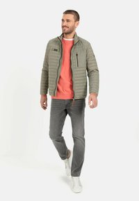 Grå pufferjakke med quiltet tekstur, lynlåslomme på brystet, over en koral sweatshirt, parret med grå jeans og hvide sneakers.