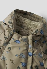 Veste beige avec une doublure douce et moelleuse. Présente un motif de dinosaures en bleu, gris et vert, avec des palmiers et des pierres. Design à capuche.