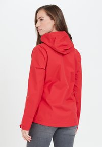 Veste imperméable rouge avec capuche ajustée, manches longues et poignets réglables. Texture lisse et design minimaliste.