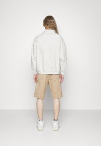 Lys grå, oversized jakke med elastisk kant, båret over beige cargo shorts. Hvide sneakers synlige. Enkel, minimalistisk design.