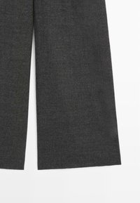 Ciemnoszare spodnie z szerokimi nogawkami z rozcięciem z przodu na każdej nodze, wykonane z grubego, teksturowanego materiału.