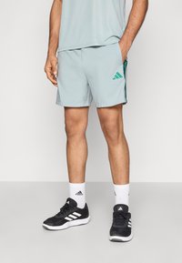 Αθλητικό σορτς ανοιχτό μπλε με πράσινη διακόσμηση τριών ρίγων, συνδυασμένο με μαύρα αθλητικά παπούτσια και λευκές κάλτσες, παρουσιάζοντας έναν απλό σχεδιασμό.