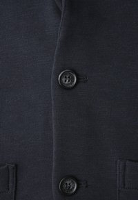 Donkerblauwe gebreide stof met twee zwarte knopen verticaal uitgelijnd en knoopsgaten, met zichtbare textuur- en stiksel details.