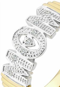 Prsteň v striebornej farbe s vystúpenými textúrovanými písmenami, čírymi kameňmi a žltým pásikom. Obsahuje detailné tvarované srdcia a geometrické akcenty.