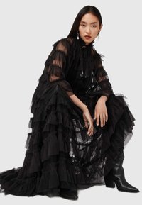 Sort tylkjole med lagdelte flæser, lange ærmer og højt halsudskæring. Sammen med høje sorte spidse støvler.