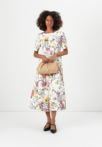 Midi dress florales con base blanca, que presenta flores coloridas en tonos púrpura, naranja y azul. Combinado con un bolso beige y zapatos planos negros.