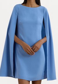 Blå mini klänning med cape ärmar, gjord av ett glatt tyg. Har en rund halsringning och diskreta sidoklipp för ökad rörelse.