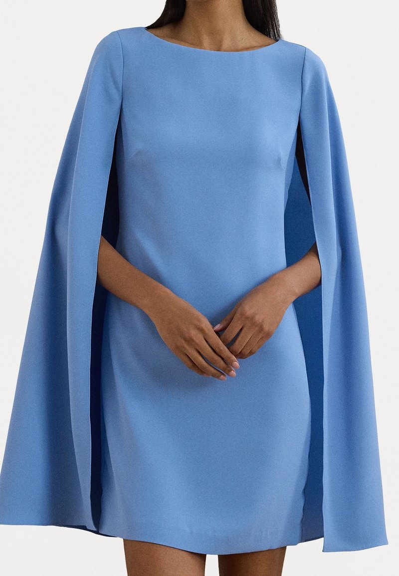 Blå mini klänning med cape ärmar, gjord av ett glatt tyg. Har en rund halsringning och diskreta sidoklipp för ökad rörelse.