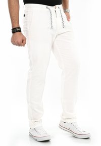 Weiße, leichte Hose mit geradem Schnitt, ausgestattet mit einem Drawstring-Bund und Seitentaschen, kombiniert mit weißen Sneakers.