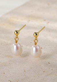 Złote kolczyki wkrętki z białymi perełkami w kształcie łzy. Posiadają gładką teksturę i prosty design, podkreślający blask pereł.
