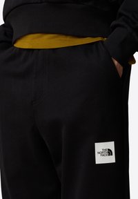 Czarne dresy wykonane z mieszanki bawełny, z teksturowanym pasem, bocznymi kieszeniami i białą łatką z logo na lewej udzie.