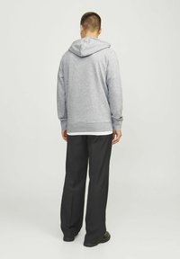Grauer Kapuzenpullover mit gerippten Bündchen und Saum, kombiniert mit schwarzen weiten Hosen, von hinten vor einem neutralen Hintergrund betrachtet.