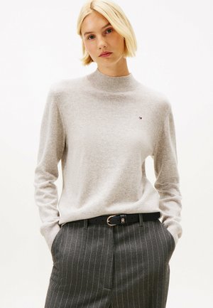 Grauer Pullover mit hohem Kragen, aus weichem Material gefertigt. Verfügt über lange Ärmel und ein kleines Logo auf der Brust. Kombiniert mit grauen gestreiften Hosen und einem schwarzen Gürtel.