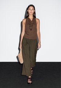 Hnědý bezrukávový top s kulatým výstřihem, doplněný volnými olivově zelenými kalhotami. Hnědé kožené sandály a světle hnědá kabelka.