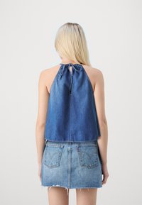 Top in denim a fascia in tessuto con una vestibilità morbida, legato al collo e con un dettaglio a chiave sul retro. Abbinato a una gonna in denim blu con orlo sfilacciato.