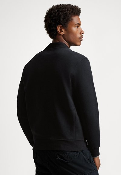 Čierna mikina z bavlnenej zmesi, s rebrovaným golierom a manžetami, hladkého textúry a minimalistického dizajnu, zobrazená zozadu.