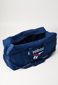 Mørkeblå duffeltaske med lynlåslukning, to bærehåndtag og skulderrem. Har et stort Reebok-logo og røde detaljer. Holdbart stof.