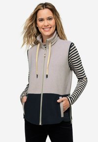 Gilet senza maniche con colletto alto, realizzato in tessuti grigi e blu navy. Presenta tasche frontali e maniche lunghe a righe sotto. Chiusura con cerniera.