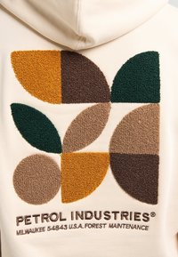 Sudadera beige con formas geométricas texturizadas y bordadas en colores verde, marrón, naranja y beige; incluye el texto "PETROL INDUSTRIES".