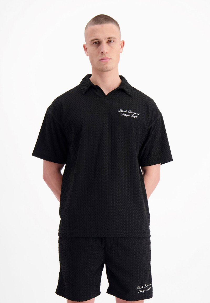 Zwart geweven shirt en short set met een textuurpatroon. Heeft een kraag en een geborduurd logo op de linkerborst.