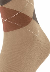 Socke mit beigen, braunen und rostfarbenen Argyle-Muster, das auf dem Knöchelbereich weiße diagonale Nähte aufweist.