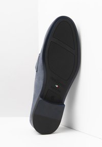 Scarpa in suede blu con suola in gomma nera, caratterizzata da una texture liscia e logo scolpito. Il tacco della scarpa è minimale e ha una forma arrotondata.