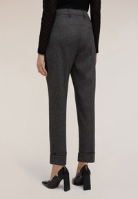 Pantalones de tweed grises con dobladillo, que cuentan con bolsillos laterales y un corte ajustado. Combinados con zapatos negros de tacón cuadrado.
