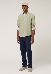 Ljusgrön långärmad polo skjorta med knäppt krage, uppkavlade ärmar, i kombination med mörkblå jeans och beigea slip-on skor.