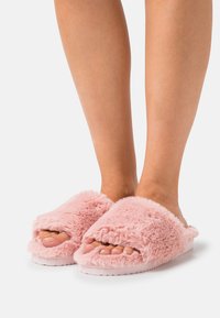 Pink fluffy slippers with an open toe design feature soft, textured fabric and a cushioned sole for comfort.