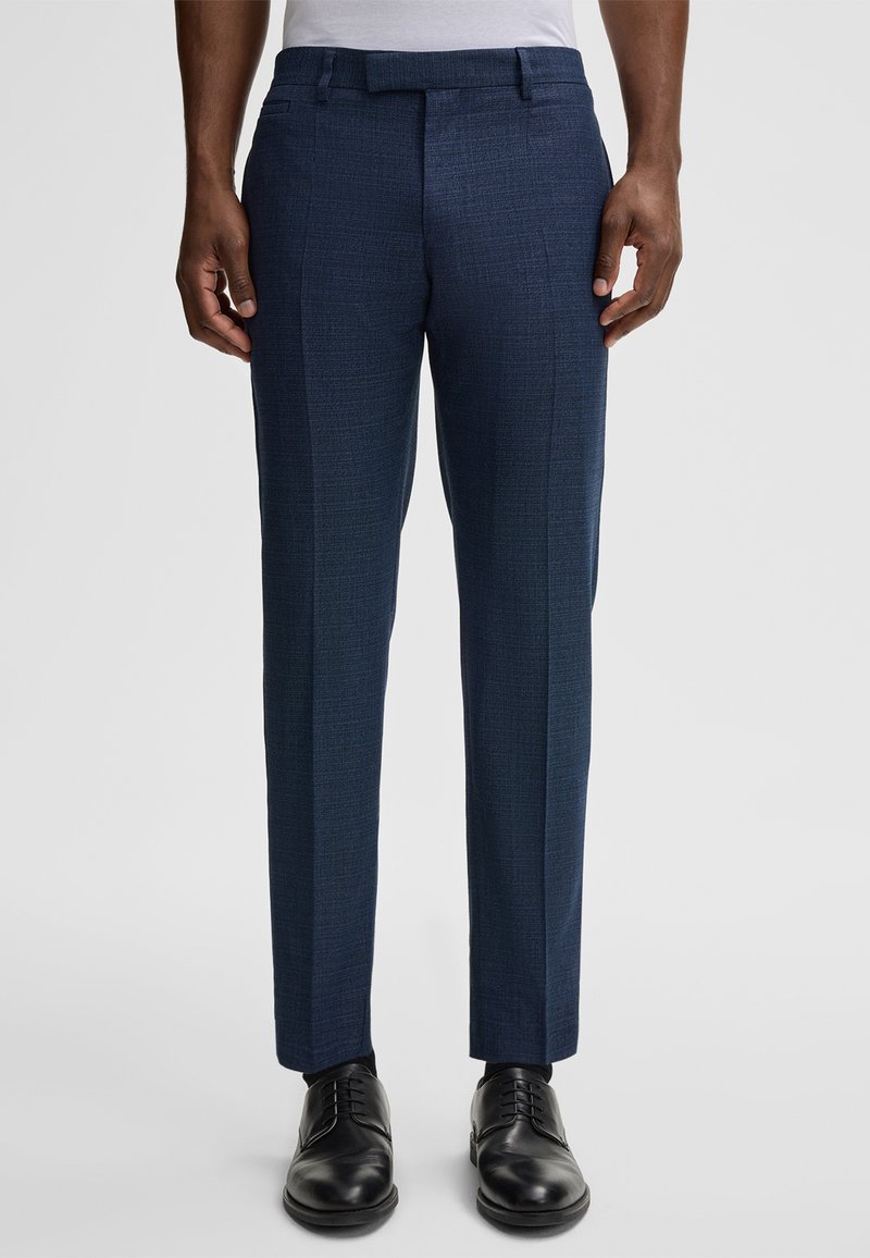 Marineblau maßgeschneiderte Hosen aus einem strukturierten Gewebe, mit flachem Bund, Seitentaschen und schmalem Schnitt, kombiniert mit schwarzen eleganten Schuhen.