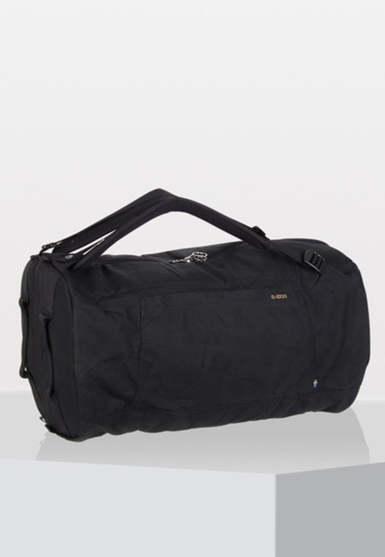 Black duffel bag made of durable fabric, cylindrical shape, zip closure, two top handles, and side pocket with a subtle logo detail.