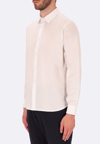 Camicia a maniche lunghe di un leggero color beige realizzata in tessuto liscio. Presenta un colletto classico, chiusura con bottoni e orlo curvo. Vestibilità sagomata.