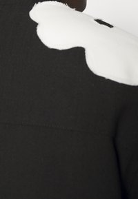 Prenda de tela negra con un gran diseño abstracto blanco en el hombro, con una superficie texturizada y detalles de costura limpios.