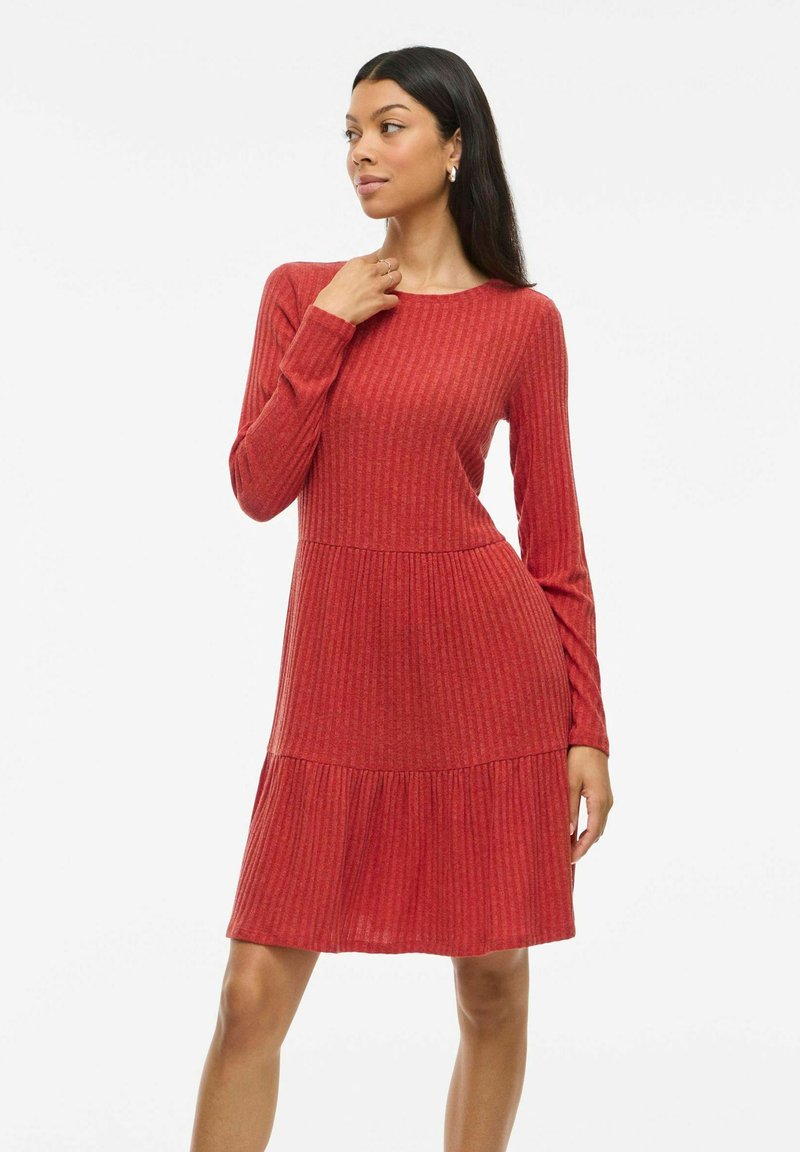 Rotes geripptes Kleid mit langen Ärmeln, rundem Halsausschnitt und gestuftem Rock. Hergestellt aus strukturiertem Stoff, mit einem taillierten Oberteil und weitem Saum.