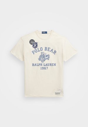 Väriltään off-white lyhythihainen T-paita, jossa sininen Polo Bear -kuvio, tekstit "POLO BEAR", "RALPH LAUREN" ja "1967", sekä kaksi tummansinistä kangasmerkkiä kauluksen läheisyydessä.