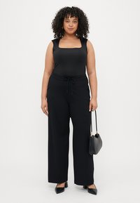 Haut sans manches noir avec un décolleté carré, associé à un pantalon noir ample avec un cordon de serrage réglable et une texture unie. Sac à main noir.