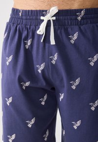 Marina blå shorts gjorda av bomull, med vita broderade fågelmönster och ett elastiskt midjeband med dragsko för justerbarhet.