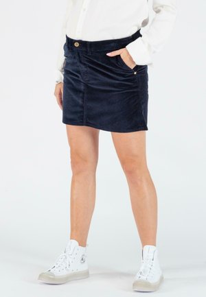 Navy corduroy mini skirt with front pockets, belt loops, and a single decorative button accent. Worn with white high-top sneakers.