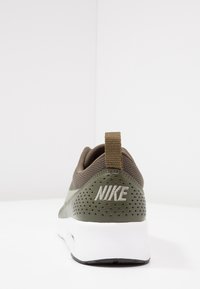 Zelená atletická teniska s perforovaným síťovaným svrškem, bílou mezipodešví a výrazným stříbrným logem Nike na patě. Texturované akcenty zvyšují přilnavost.