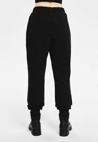 Czarne spodnie dresowe wykonane z miękkiego materiału, wyposażone w elastyczny pas i ściągacze przy kostkach. Zaprojektowane z luźnym krojem.