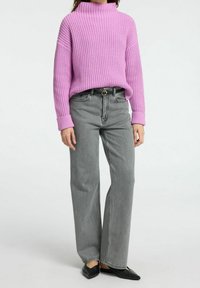 Pull rose côtelé à col montant associé à un jean gris à jambes larges, complété par des ballerines noires à bout pointu. Tricot texturé et coupe décontractée.