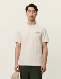 Beige színű pamut póló, rövid ujjú, kerek nyakkivágással, zöld "LES DEUX" grafikai szöveggel a bal mellrészen. Egyszerű dizájn, puha tapintás.