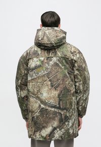 Giacca imbottita con motivo mimetico che presenta tonalità di marrone, verde e grigio. Include un cappuccio e una tasca posteriore con cerniera.