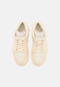 Baskets de basketball beige clair avec un design en cuir perforé, des accents roses et une languette en mesh texturé. Elles comportent un laçage traditionnel.