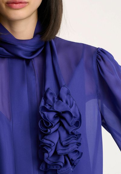 Paarse chiffon blouse met een gerimpeld sjaaldetail, een zachte textuur en puffed mouwen voor extra nadruk.